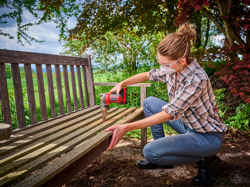 A woman fixing a wooden bench with an Einhell tool. 