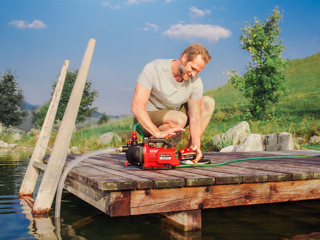 Un homme retire la batterie Power X-Change de la pompe de jardin Einhell AQUINNA.