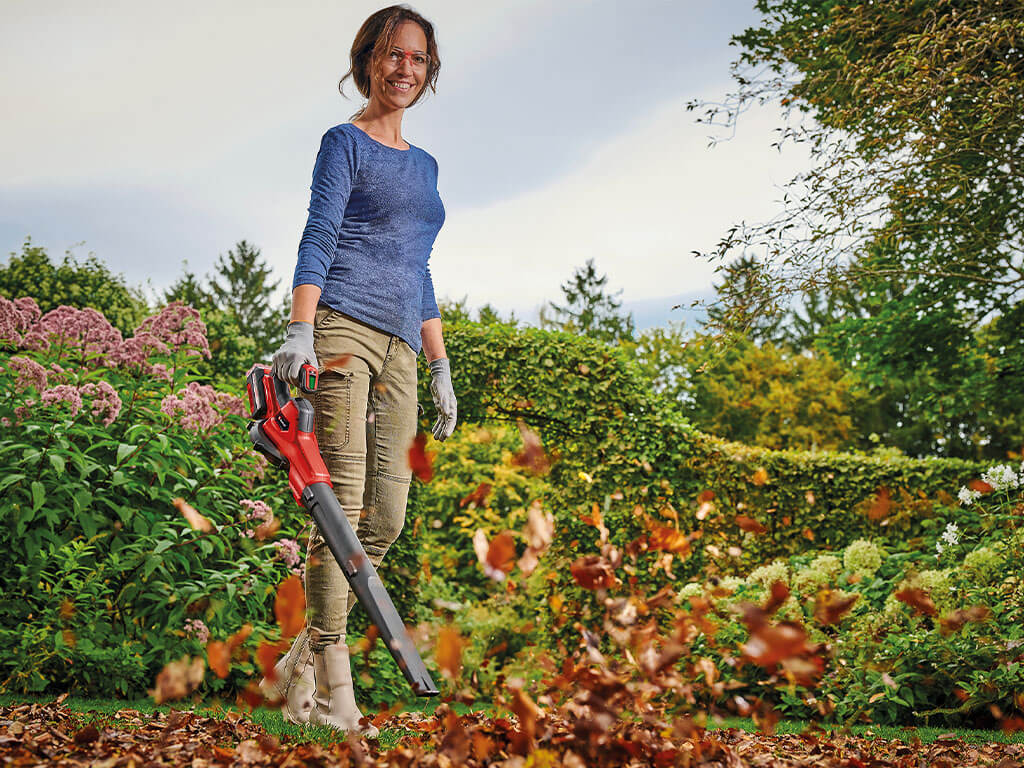 A woman raking up leaves in her yard with an Einhell cordless leaf blower.