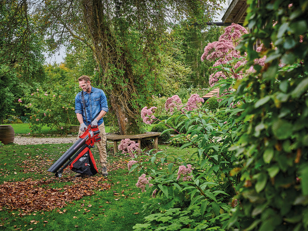 A man freeing his garden from autumn leaves with the help of an Einhell leaf vacuum cleaner.