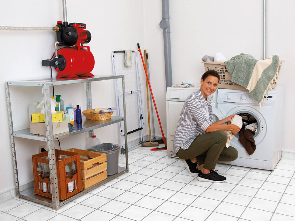 A woman smilingly fills the washing machine connected to an Einhell domestic waterworks.