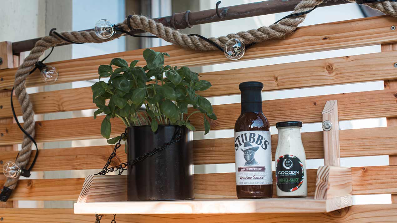 A basil pot and two condiment sauces are placed on a hanging shelf