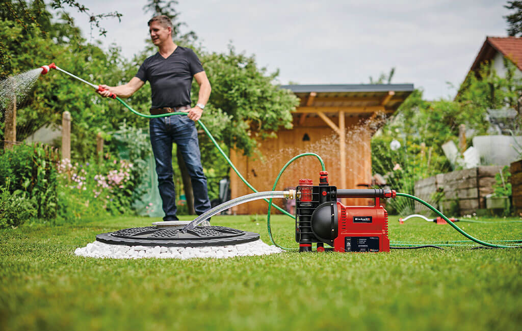 A man watering flowers in his garden with rainwater and the help of a garden pump.