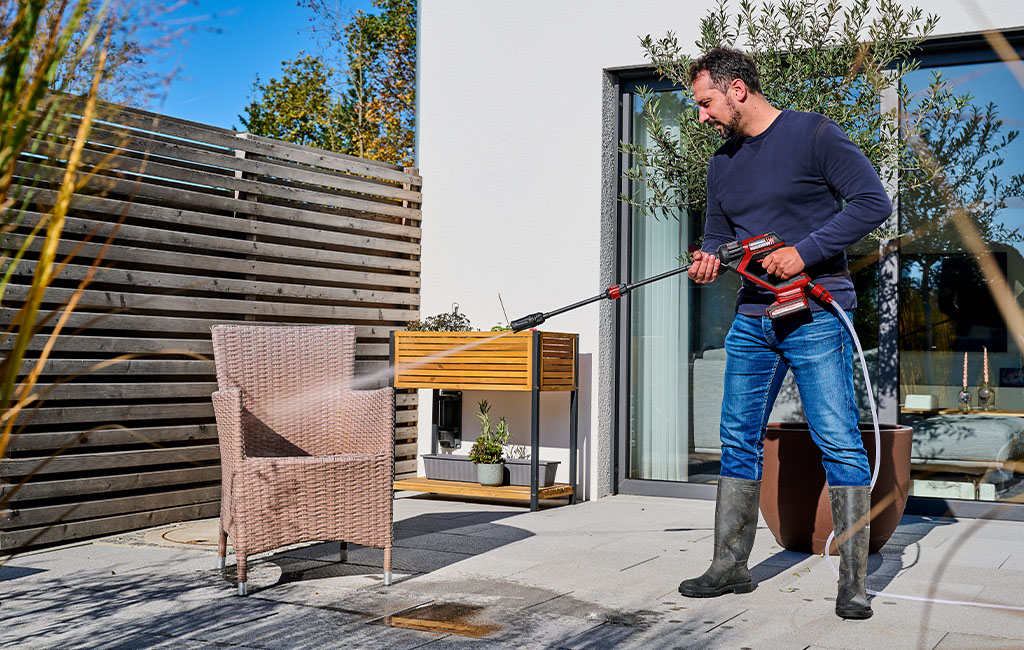 A man cleaning a rattan garden chair with a cordless pressure washer on a patio