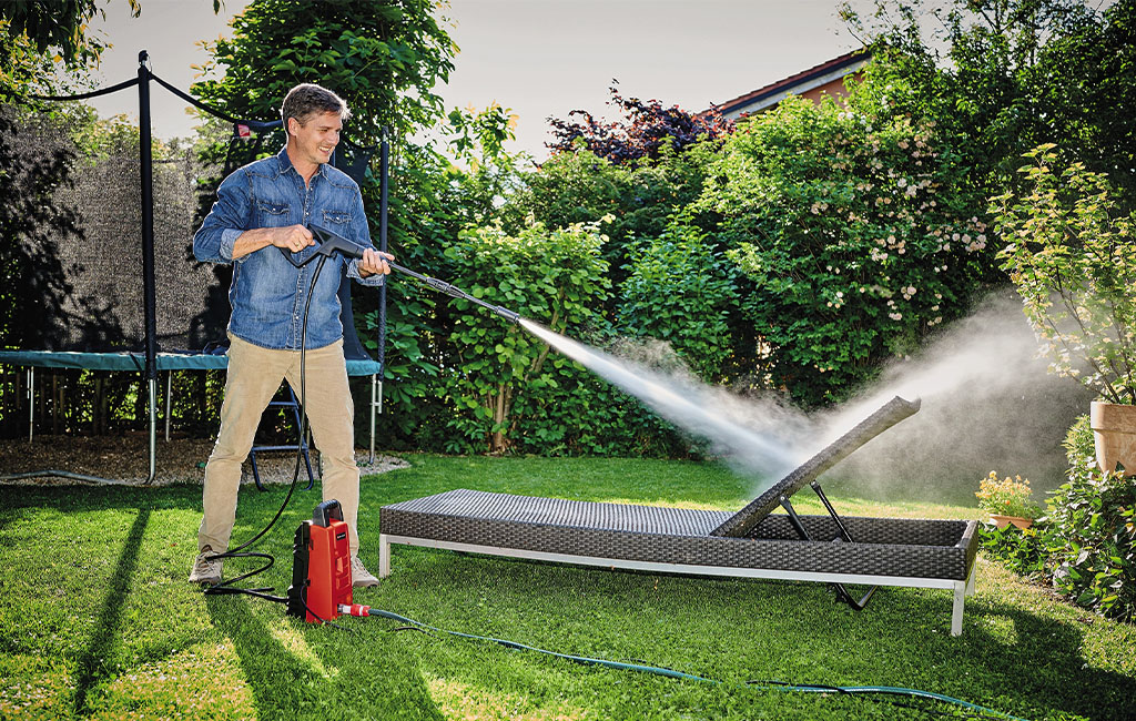 Man in the garden cleaning a garden lounger with the help of an Einhell high-pressure cleaner