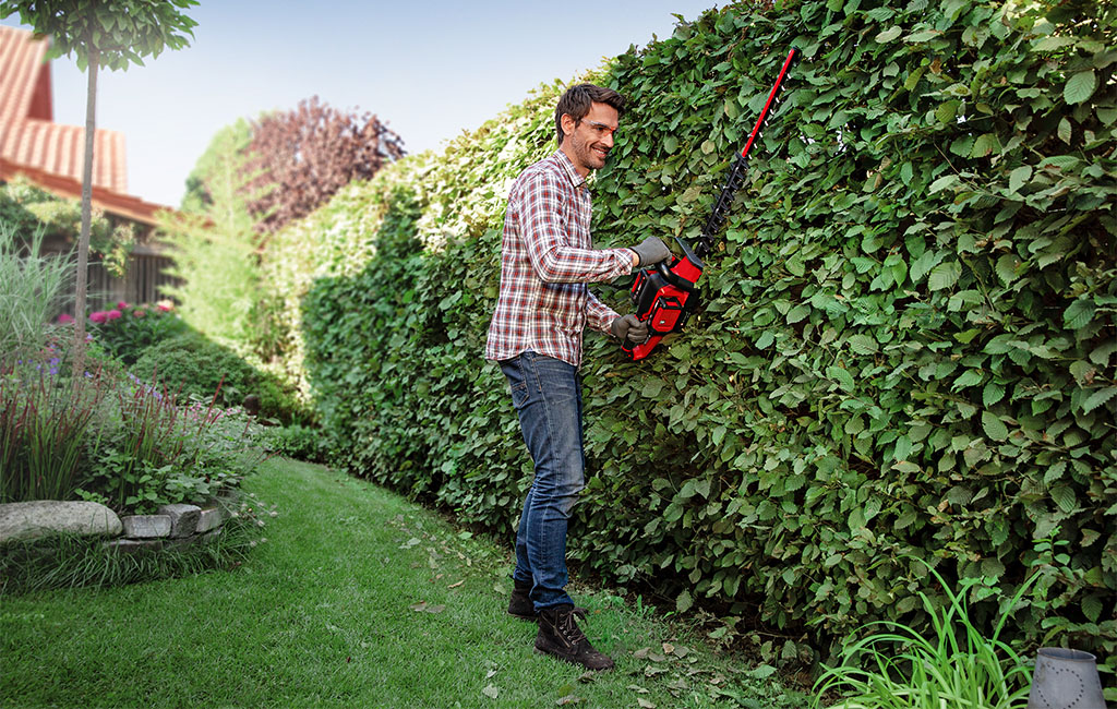 a man is trimming a hedge with a Einhell hedge trimmer