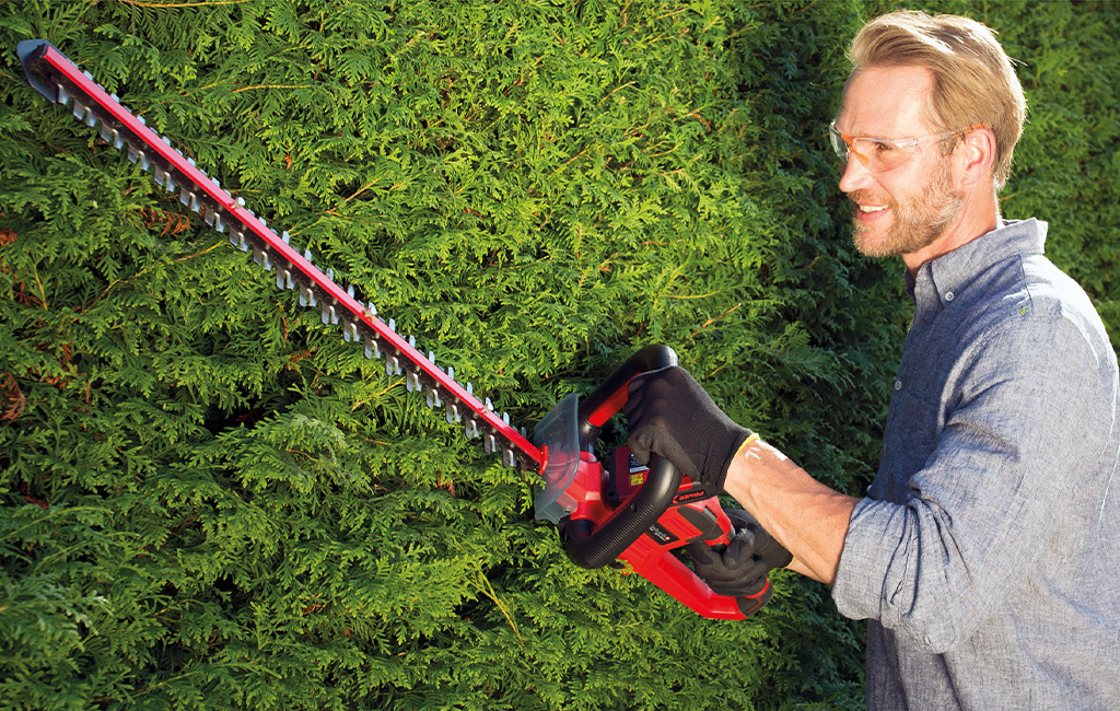 a man is trimming a hedge with a Einhell hedge trimmer