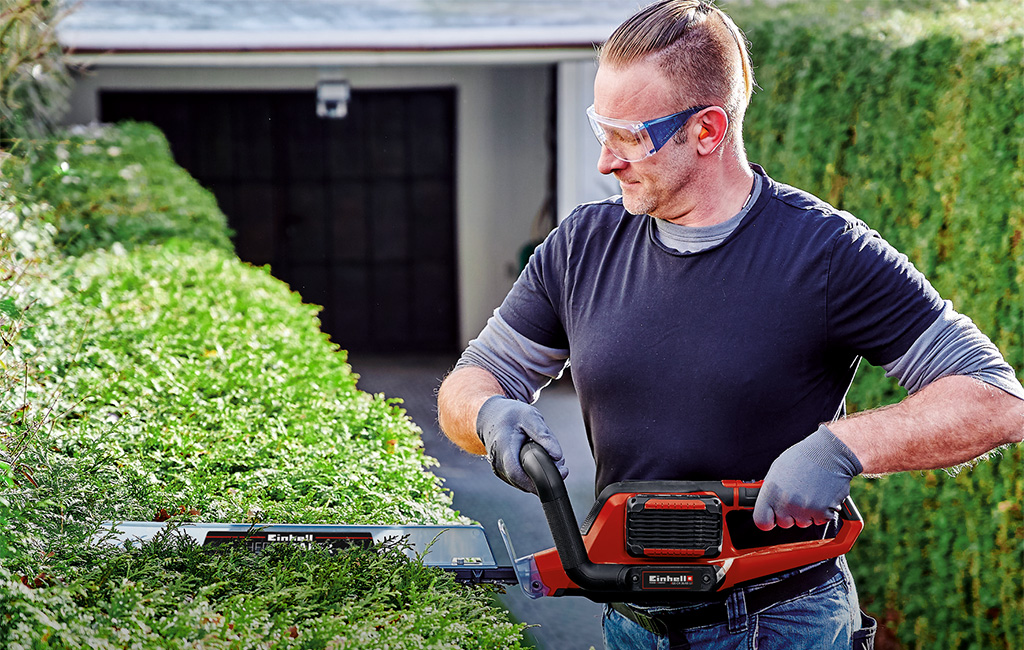 a man is trimming a hedge with a Einhell hedge trimmer