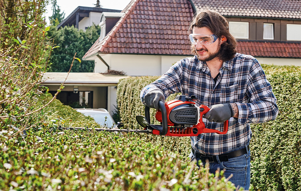 a man is trimming a hedge with a Einhell hedge trimmer