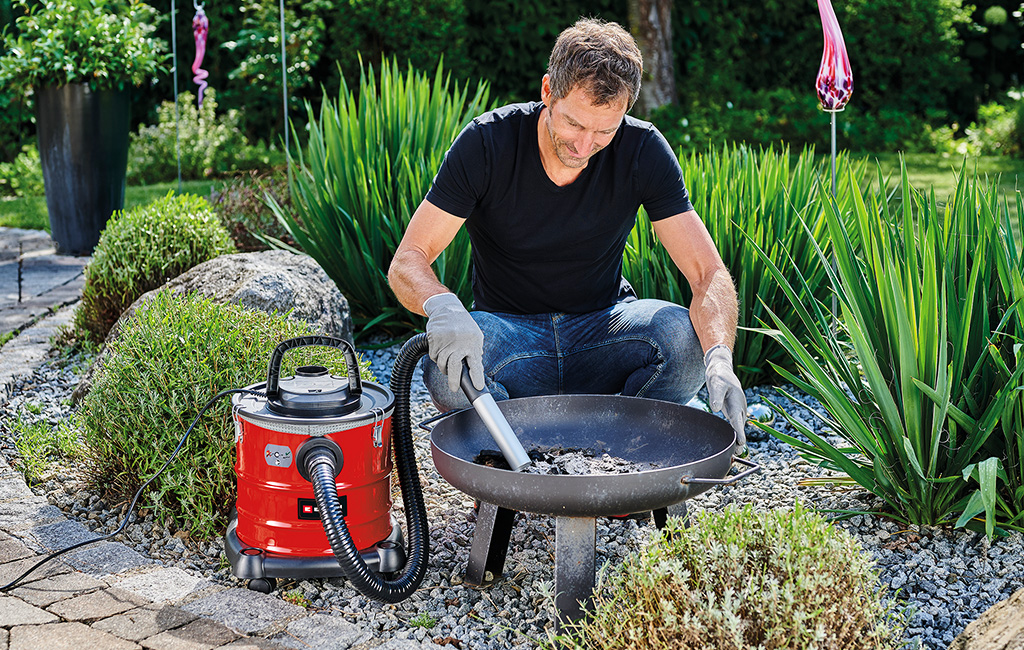 A man is collecting cooled ashes from a grill using an einhell ash vacuum cleaner