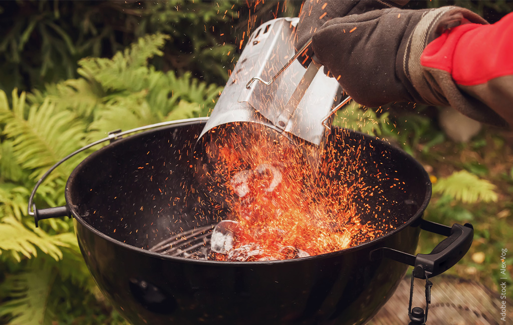 Someone is pouring hot charcoal into a grill