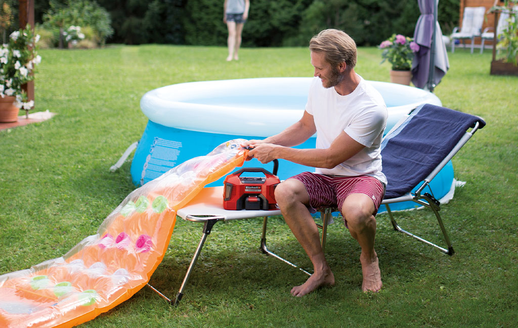 A man is inflating an air mattress with the Einhell Hybrid-Compressor PRESSITO