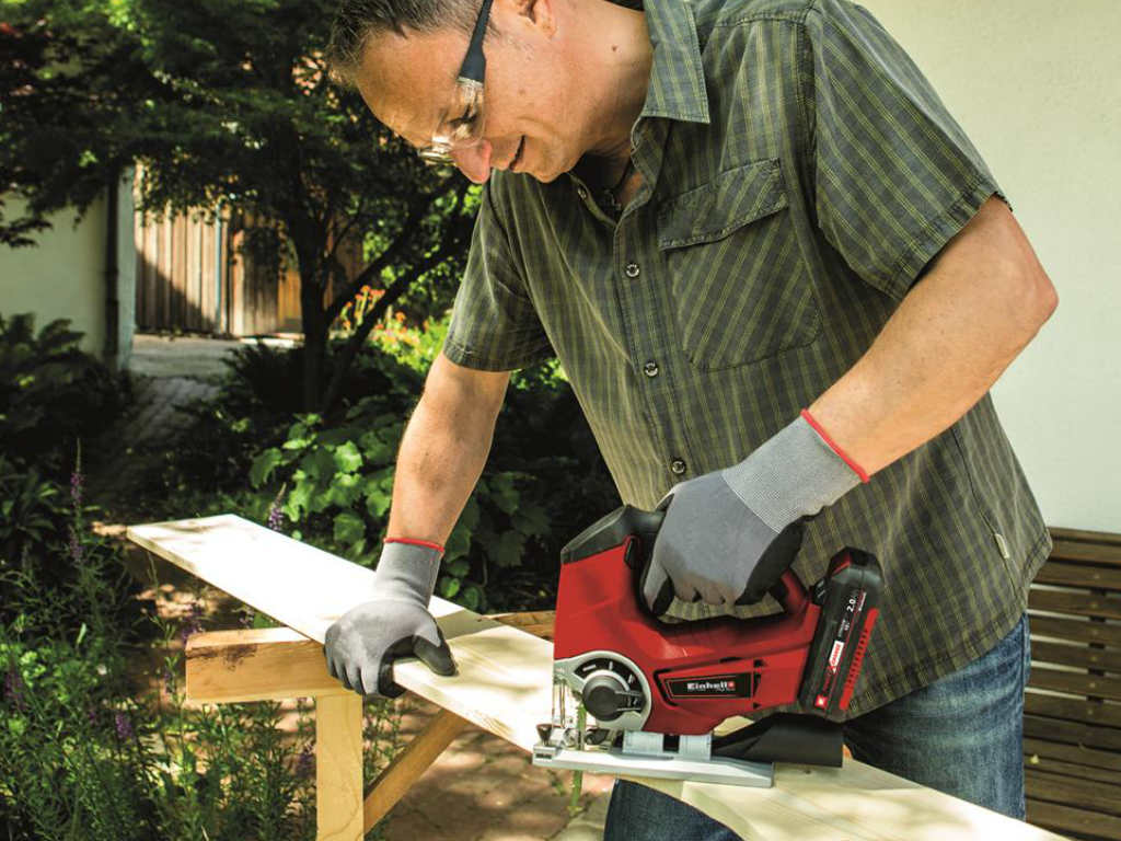 A man cutting out a piece of wood with the cordless jig saw. 