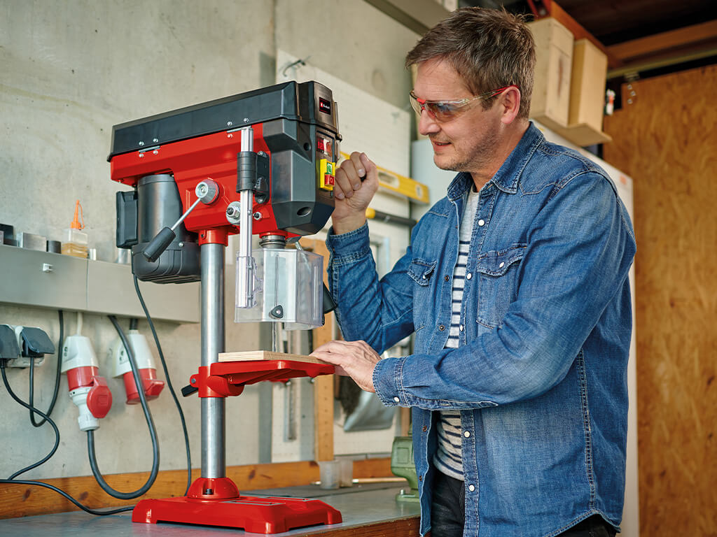 Man working on an Einhell bench drill to drill into a wooden panel.