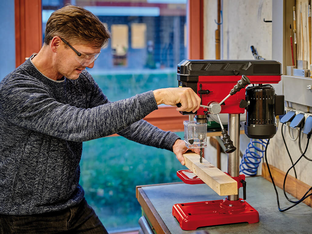 Man moving the drill spindle of a bench drill down to drill into a piece of wood.