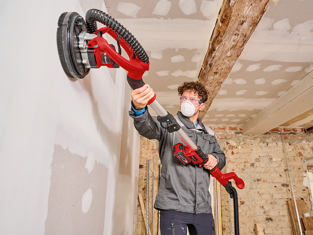 Mann mit Akku-Trockenbauschleifer schleift Trockenbauwand auf Baustelle