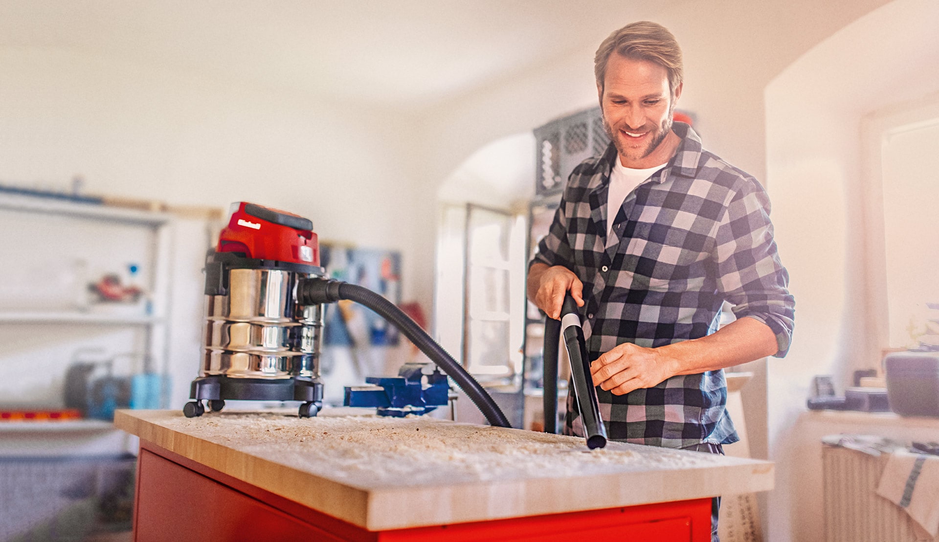 A man using the wet-dry vacuum cleaner in his workshop. 