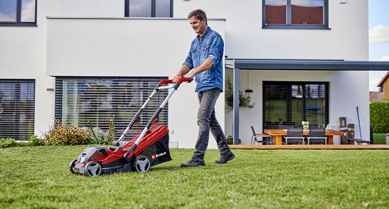 A man mowing the green grass in his garden with a cordless lawnmower.