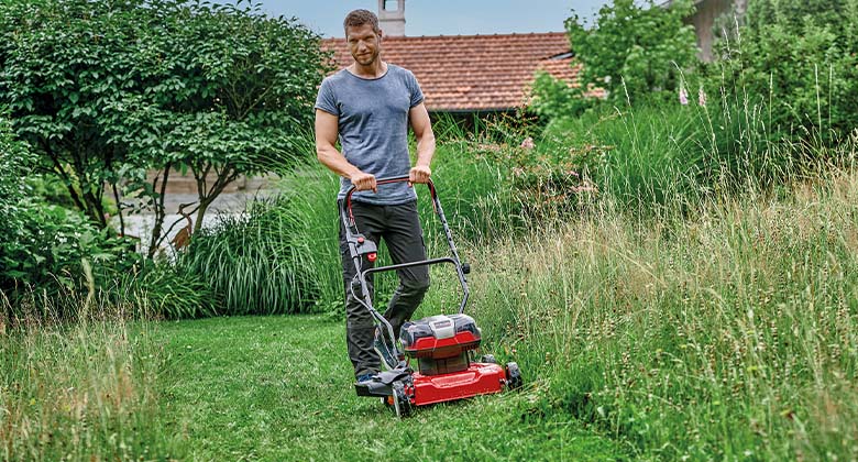 A man mowing tall grass in a meadow with a cordless mulching mower.