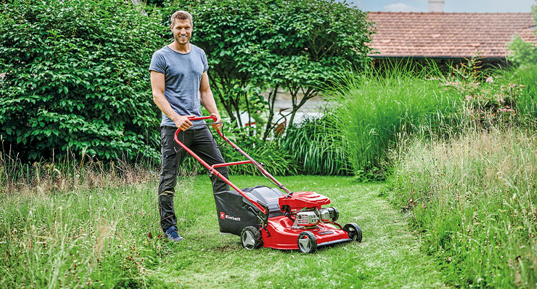 A man standing with a petrol lawn mower in the garden. 