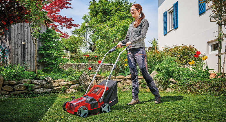 A woman scarifying the lawn in the garden in front of a house.