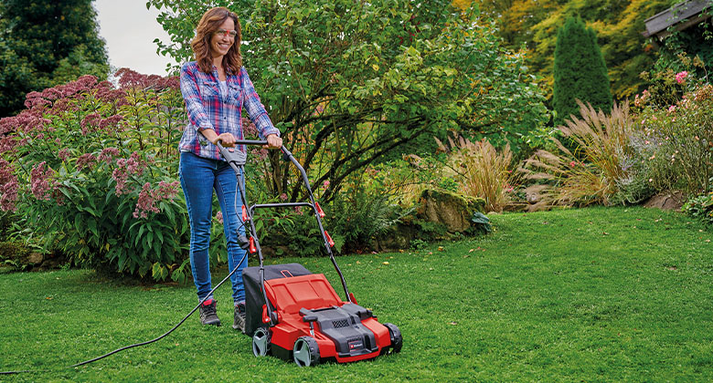 A woman with a scarifier tending the lawn in the garden.